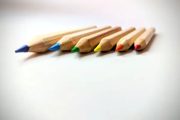 Six crayons de couleur posés côte à côte sur une table blanche