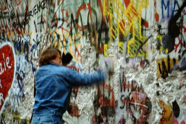 Un homme de dos frappe le mur de Berlin couvert de graffitis, en 1989